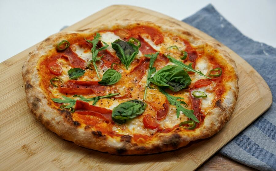 Pizza Diavola mit Basilikum auf Holzbrett