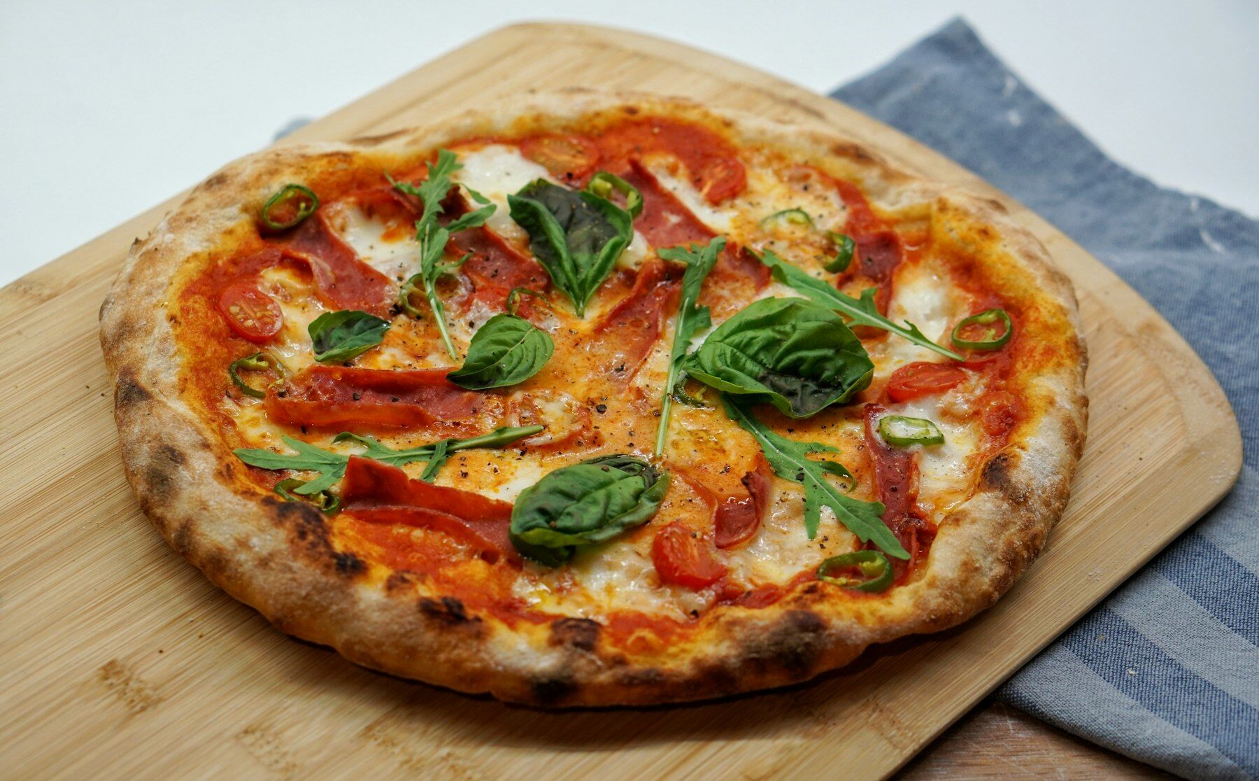 Pizza Diavola mit Basilikum auf Holzbrett